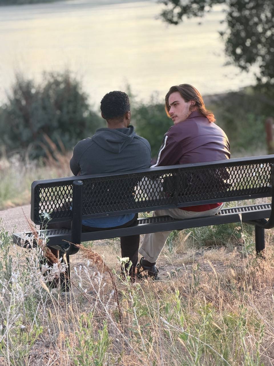 Two men on a park bench seen from behind, one glancing back